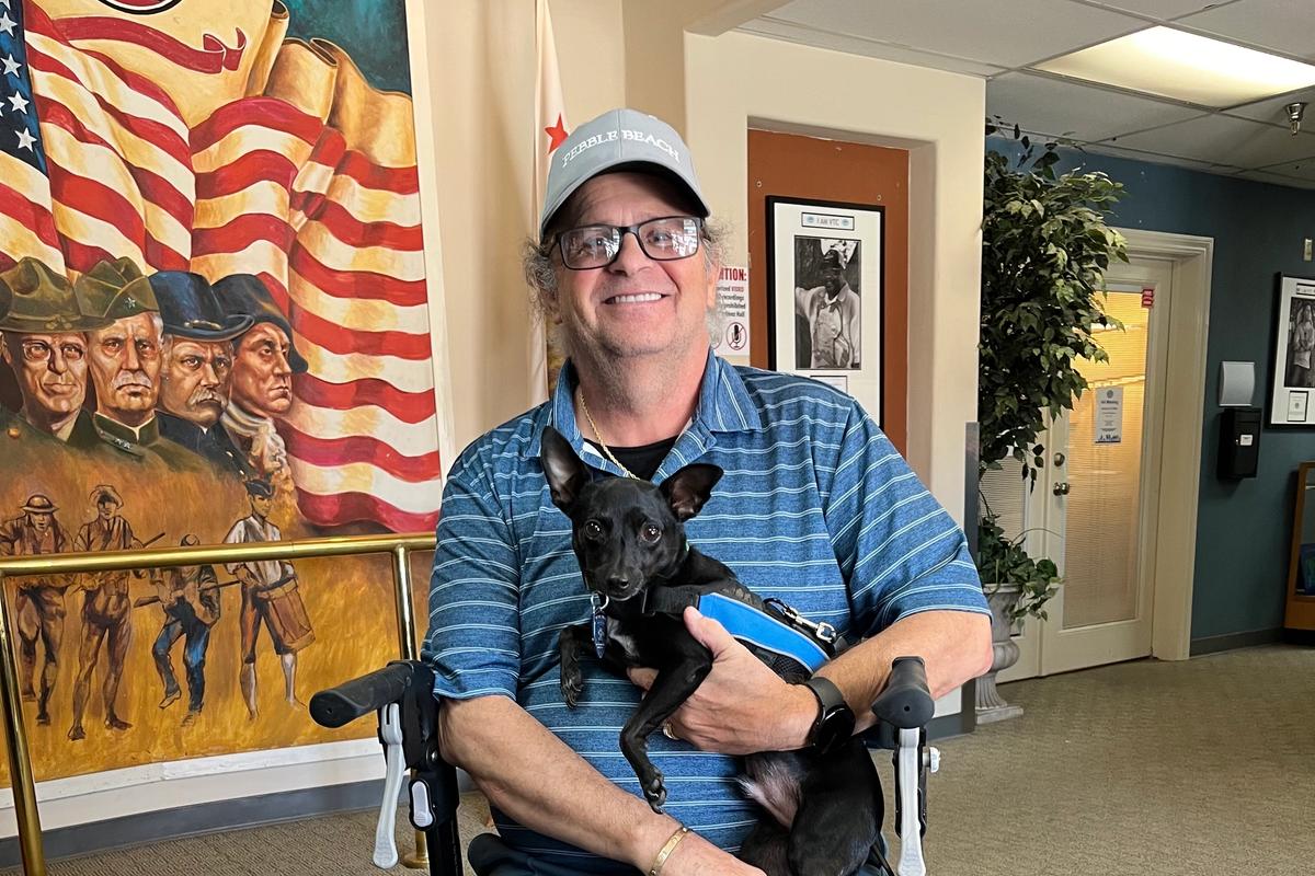 A Veteran seated in a wheelchair holding a small black service dog in the VTC lobby