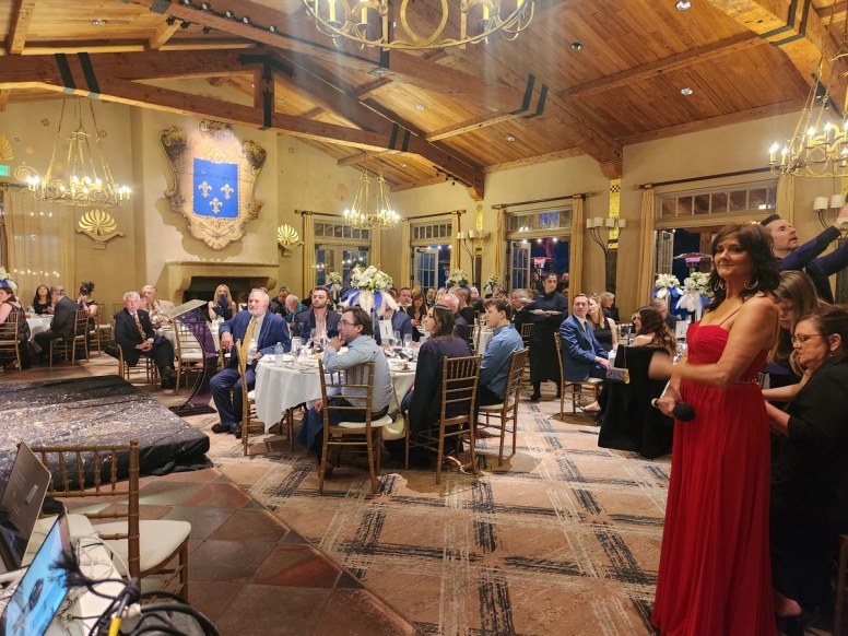 A vocalist in a red gown performs for seated guests in the gala's candlelit dinner ballroom