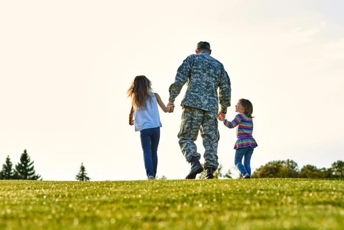 A Veteran in uniform walking outdoors at sunset holding hands with two young children