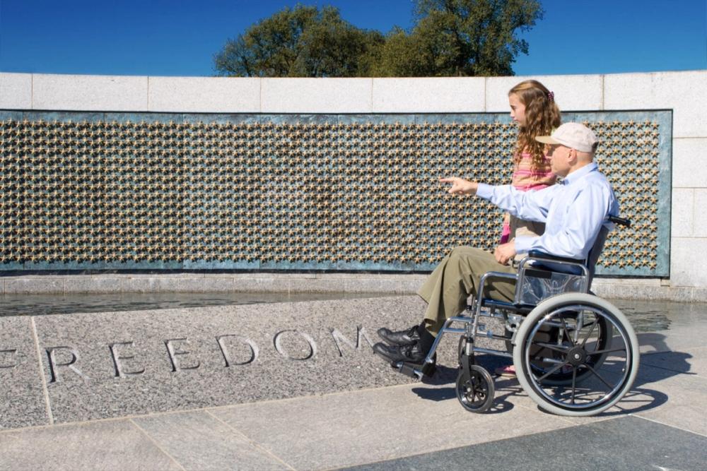 A Veteran in a wheelchair and a young girl at the World War II Memorial Freedom Wall