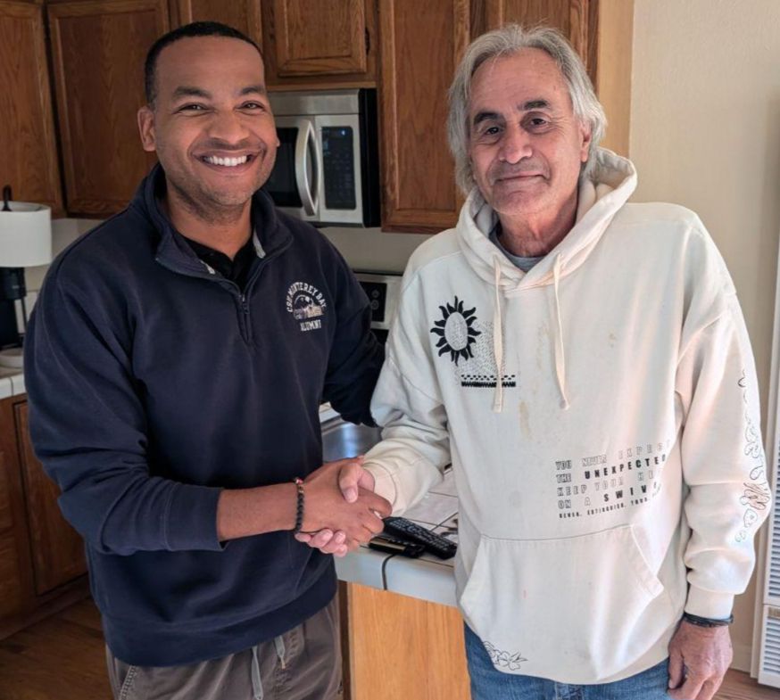 Two men smile and shake hands in a home kitchen