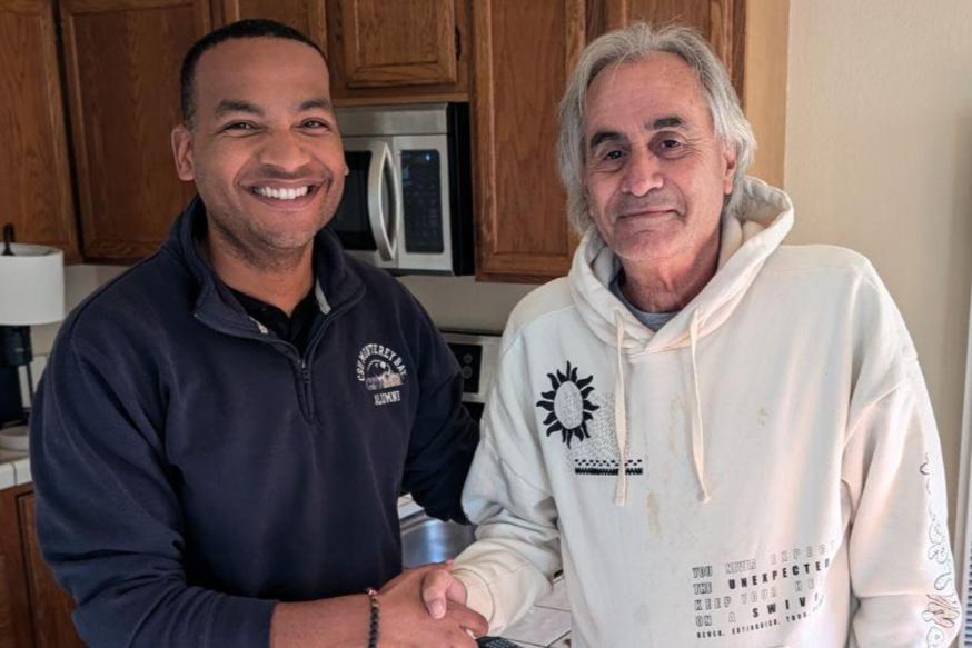 Two men smile and shake hands in a home kitchen