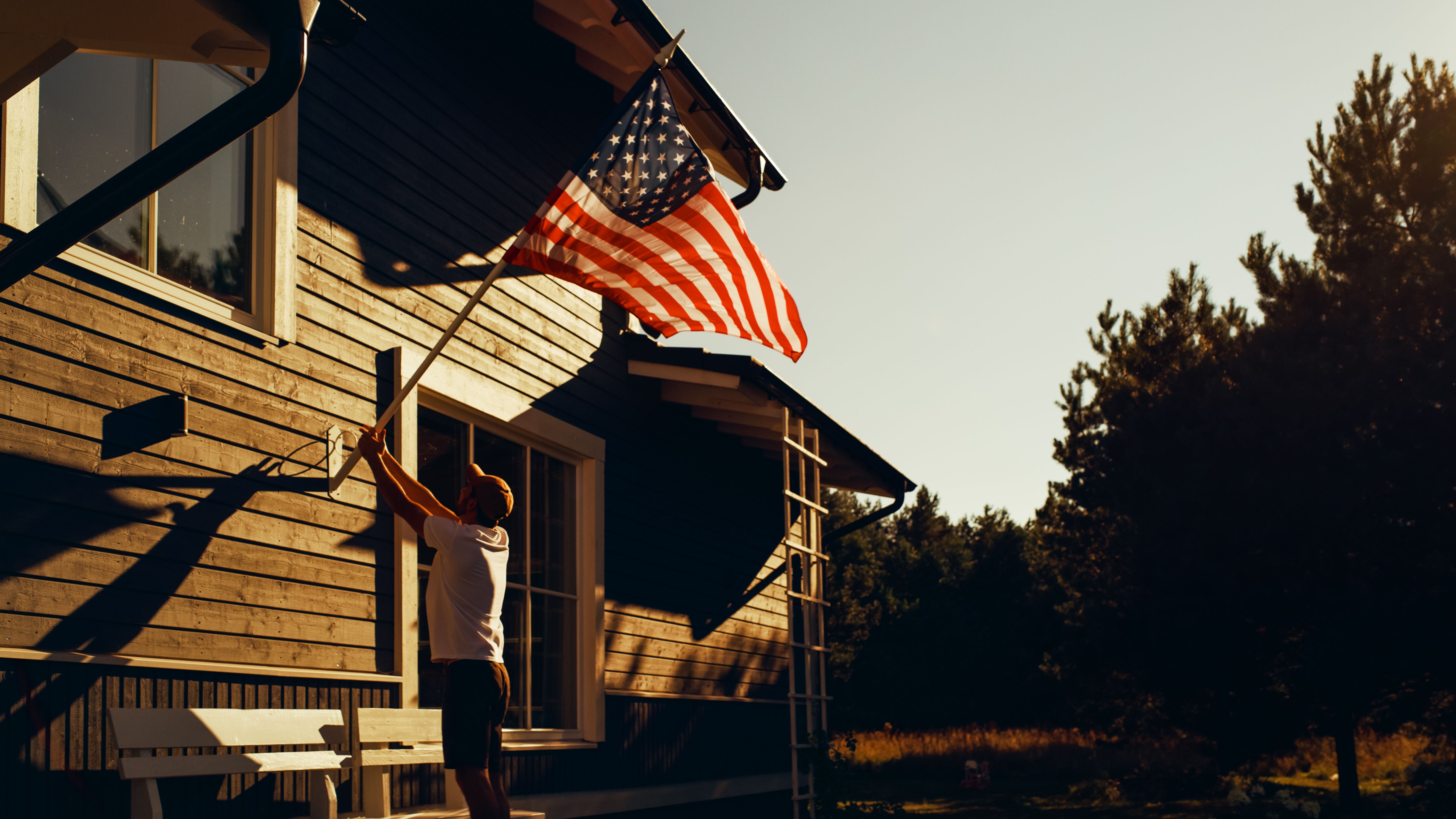 A man raises the American flag on his home at golden hour