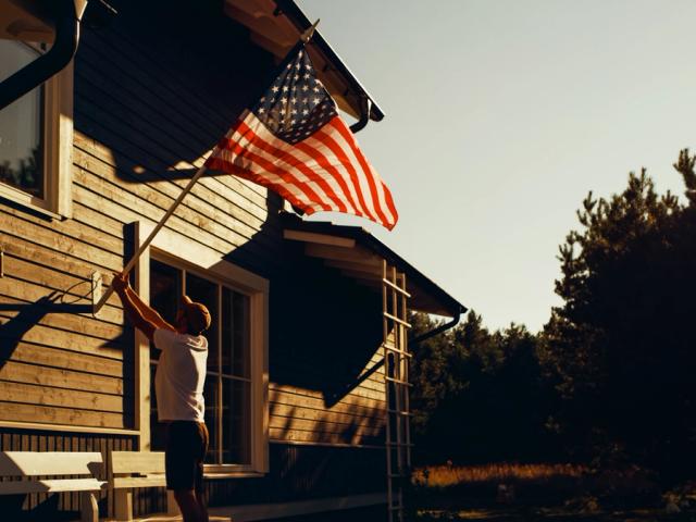 A man raises the American flag on his home at golden hour