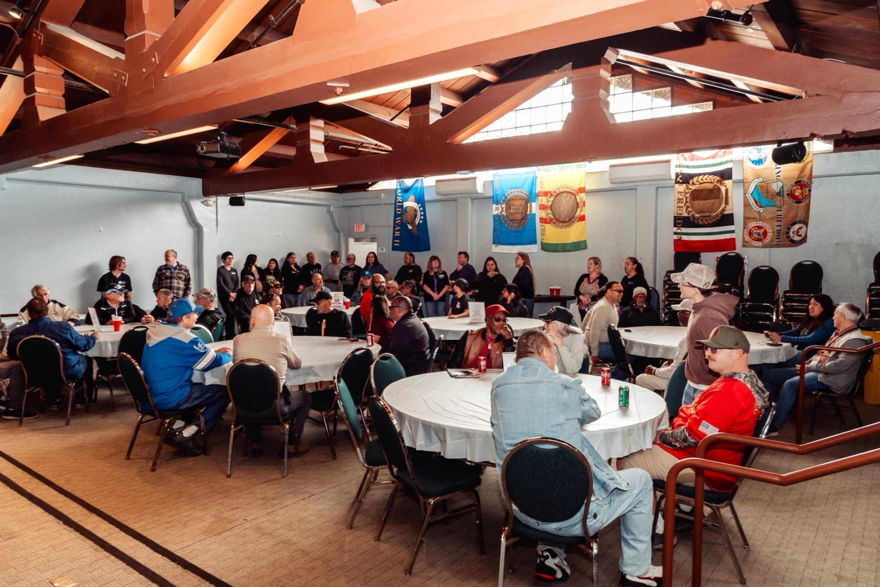 Veterans gathered around round tables in the historic Fort Ord hall, service-era flags hanging along the wall