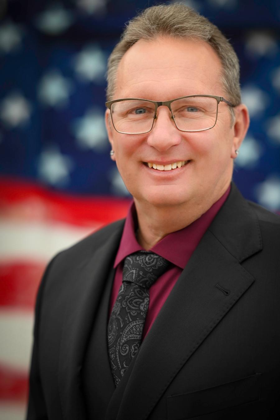 Craig Linfoot in a suit in front of the American flag