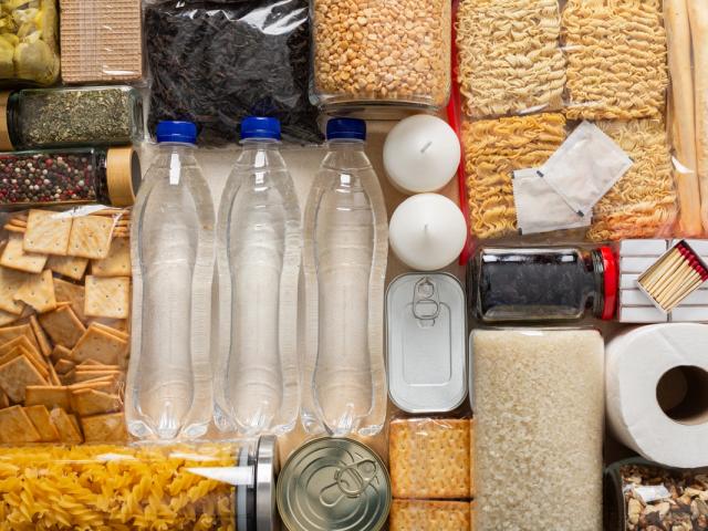 Pantry staples laid out — water, rice, pasta, canned goods, and essentials