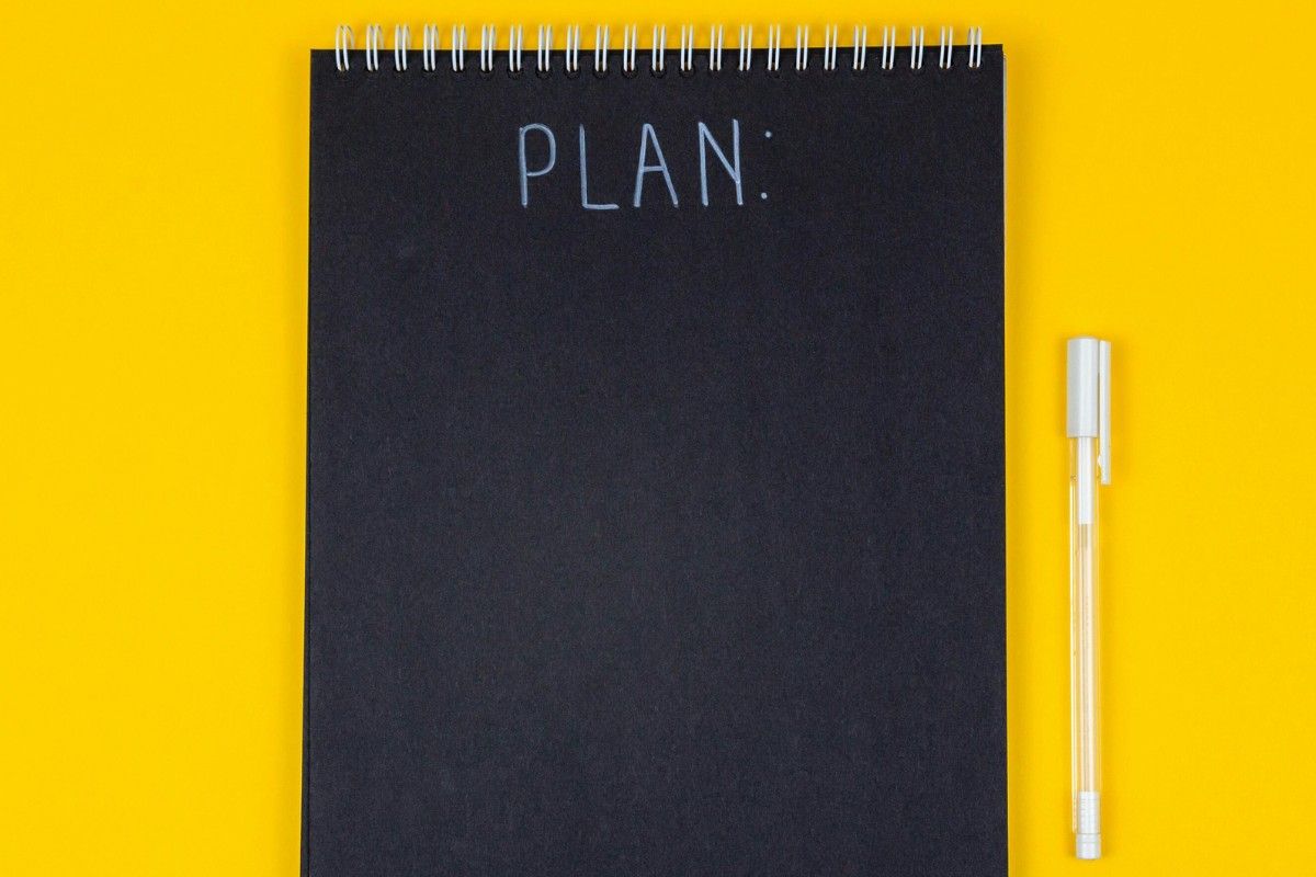 Notizblock mit Schriftzug "Plan" auf gelben Hintergrund mit weißem Stift