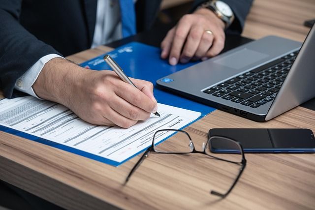 brille liegt auf tisch laptop handy und mann schreibt etwas