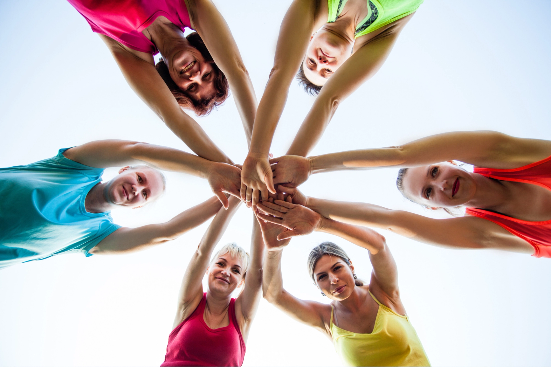 Frauen in Sportkleidung, die gemeinsam die Hände zur Mitte strecken