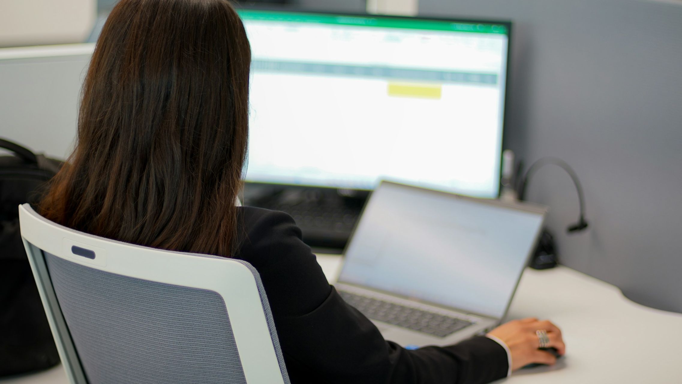 Frau sitzt auf einem Bürostuhl vor 2 Bildschirmen und arbeitet