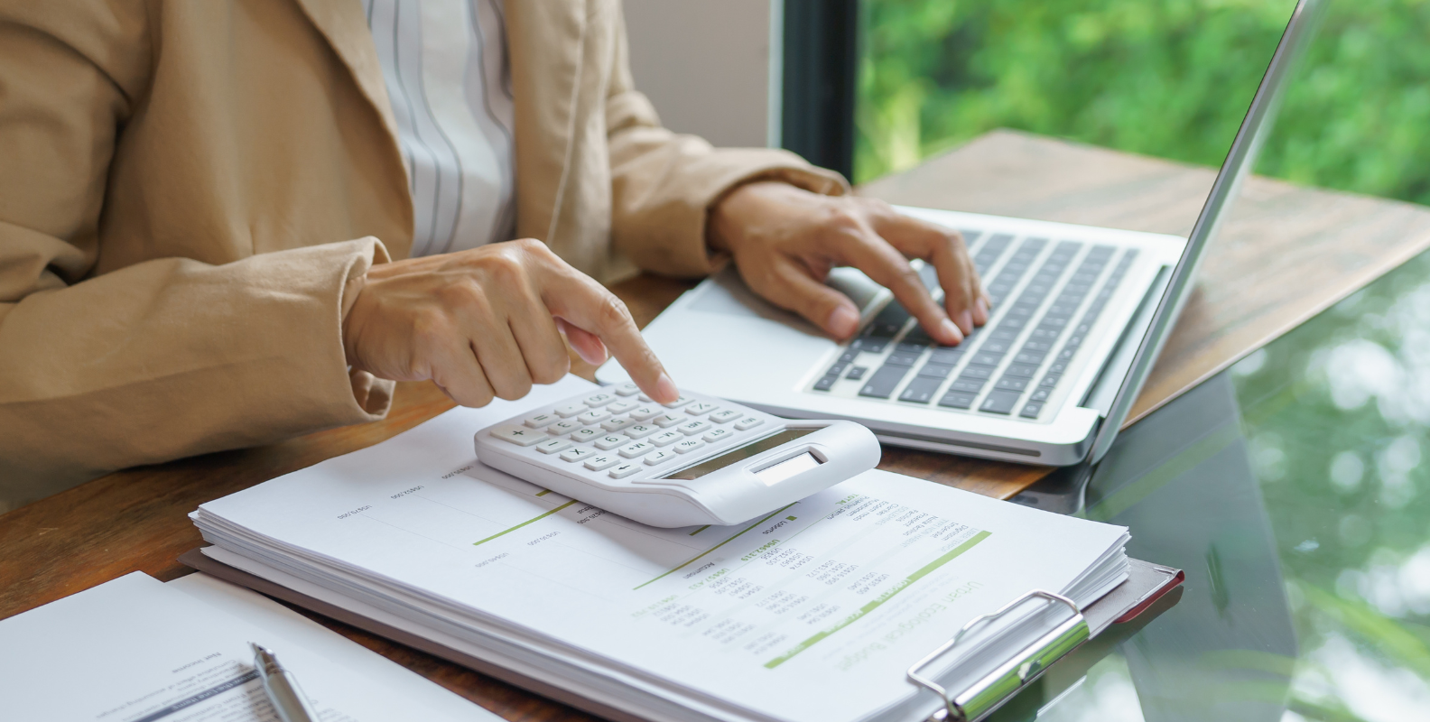 Eine Frau sitzt am Computer und macht Buchhaltung mit einem Laptop und einen Taschenrechner