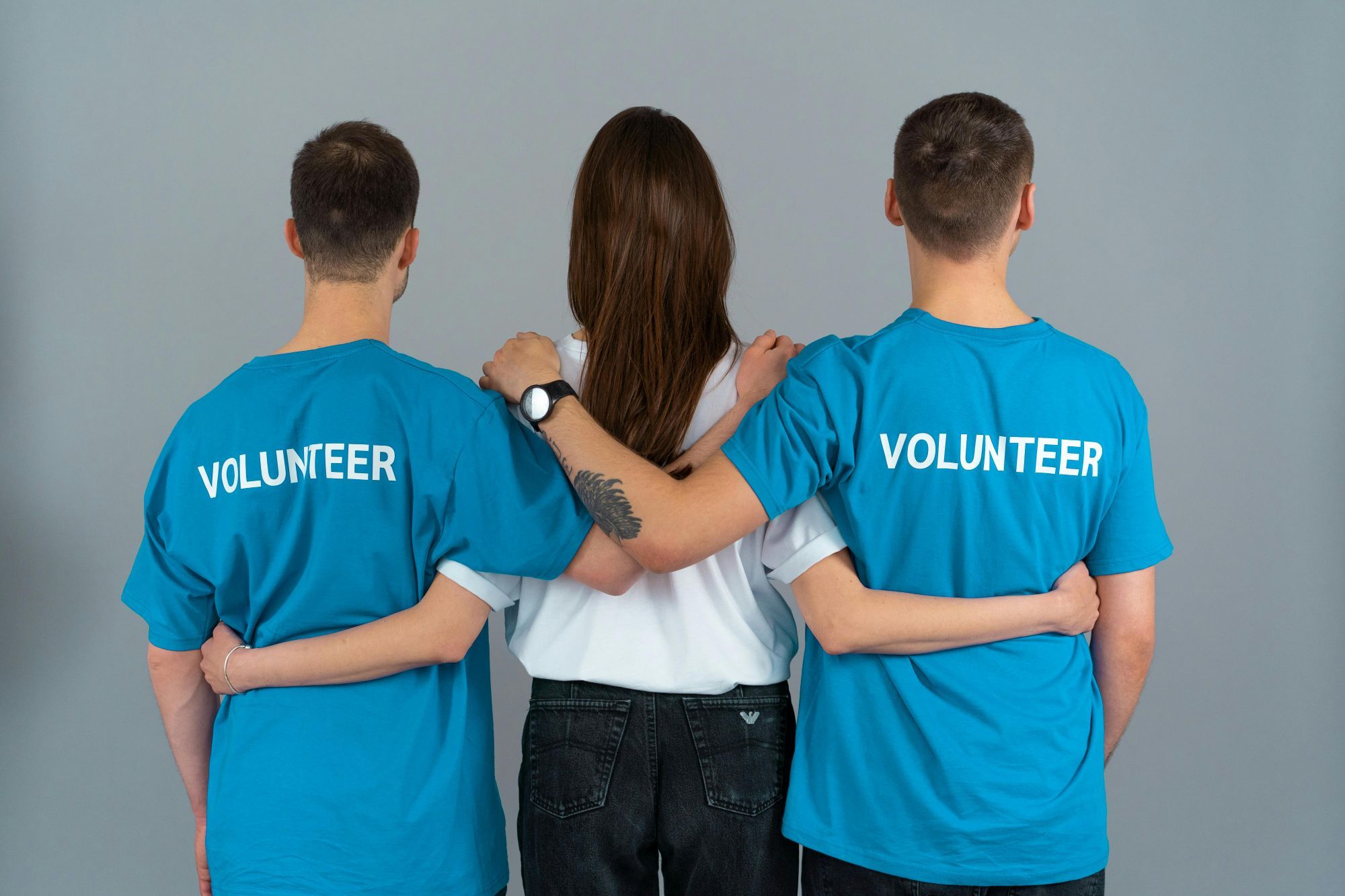 Drei Personen stehen Rücken an Rücken mit verschränkten Armen, zwei tragen T-Shirts mit der Aufschrift „Volunteer“ - engagierte Helfer in einem Förderverein.