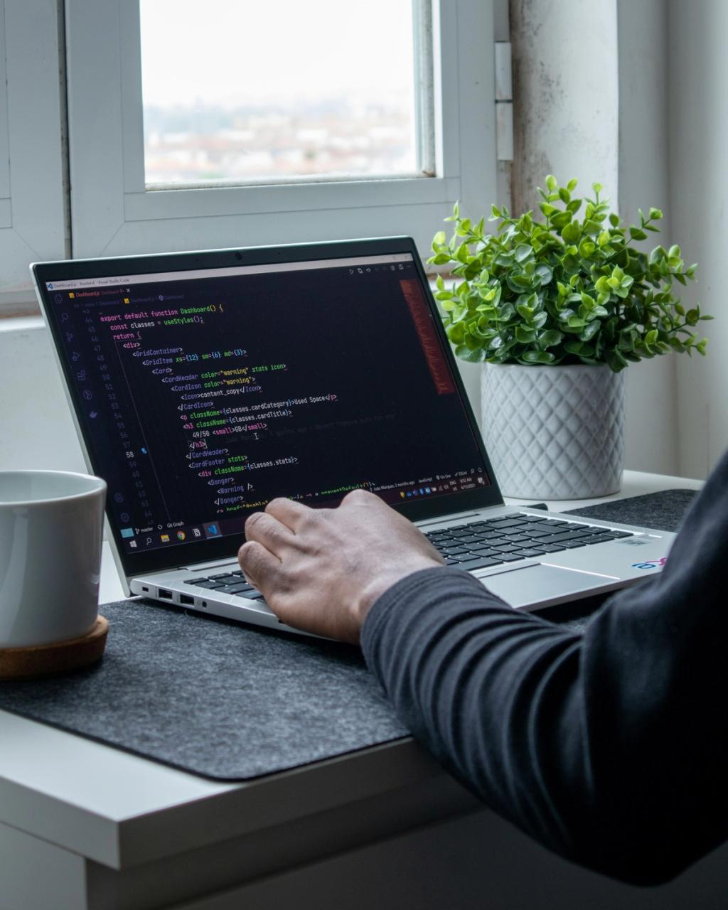 Laptop auf Tisch mit einer Pflanze und einem Arm, der den Laptop bedient