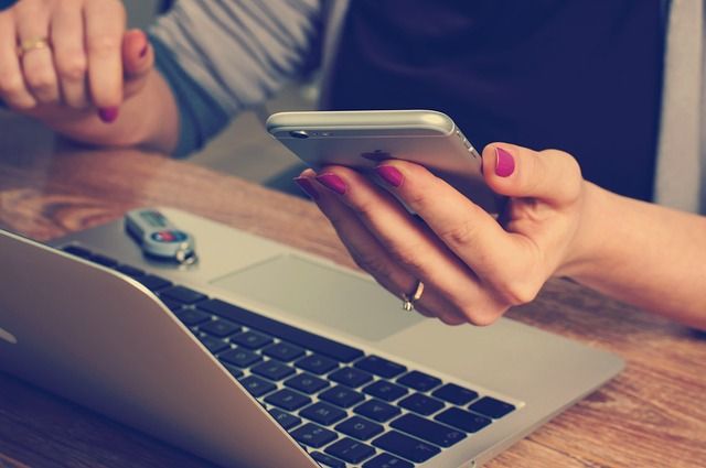 Am Laptop sitzen und auf das Smartphone schauen