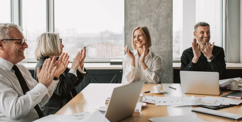 Mitglieder einer Genossenschaft sitzen an einem Tisch und klatschen in die Hände