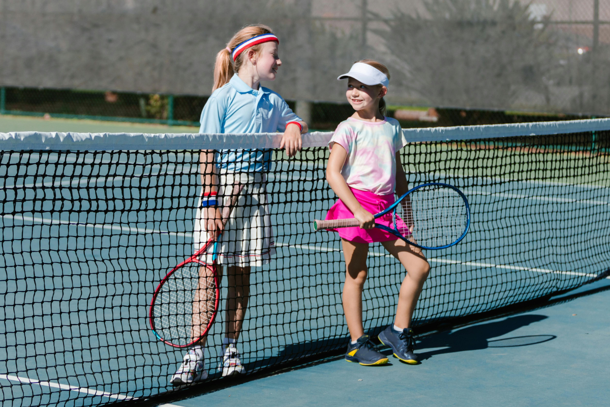 Zwei junge Mädchen stehen auf einem Tennisfeld im Verein. Beide halten einen Tennisschläger in der Hand.