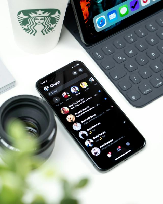 An image of an iphone next to a laptop, a camera lens, and a starbucks cup