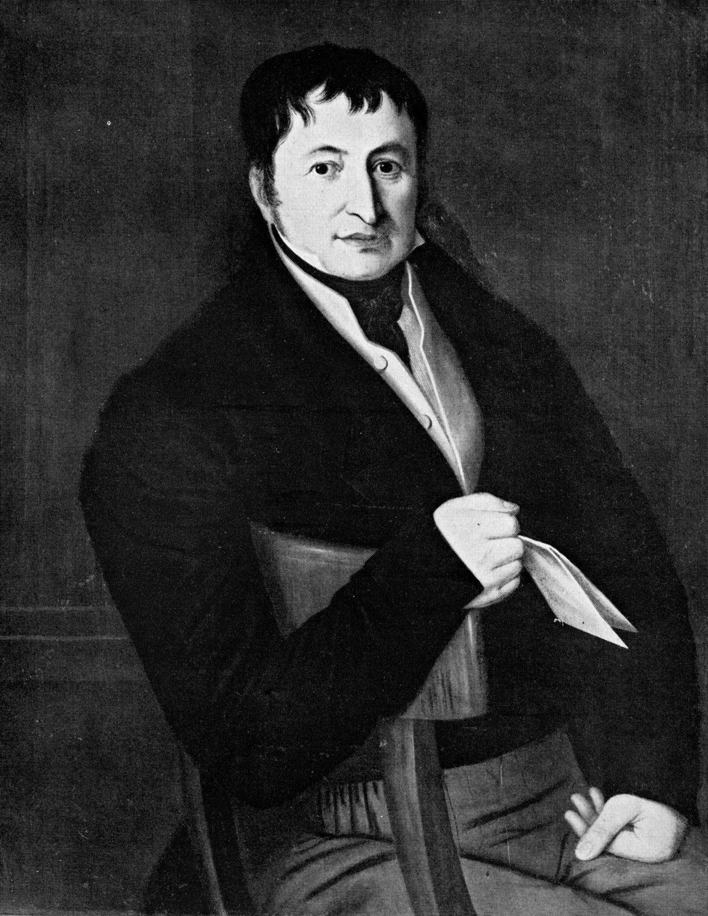 Black-and-white portrait of a seated man with short dark hair, in a dark coat and high white collar, holding a folded paper