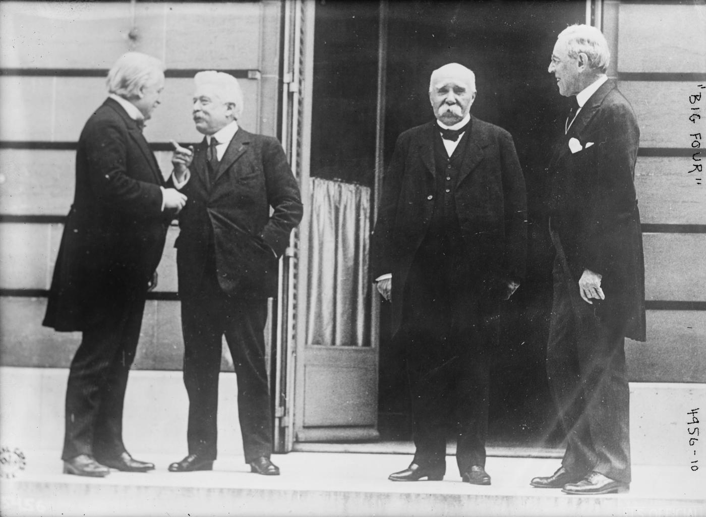 Black-and-white photograph of four older men in dark suits standing together outside the doorway of a stone building