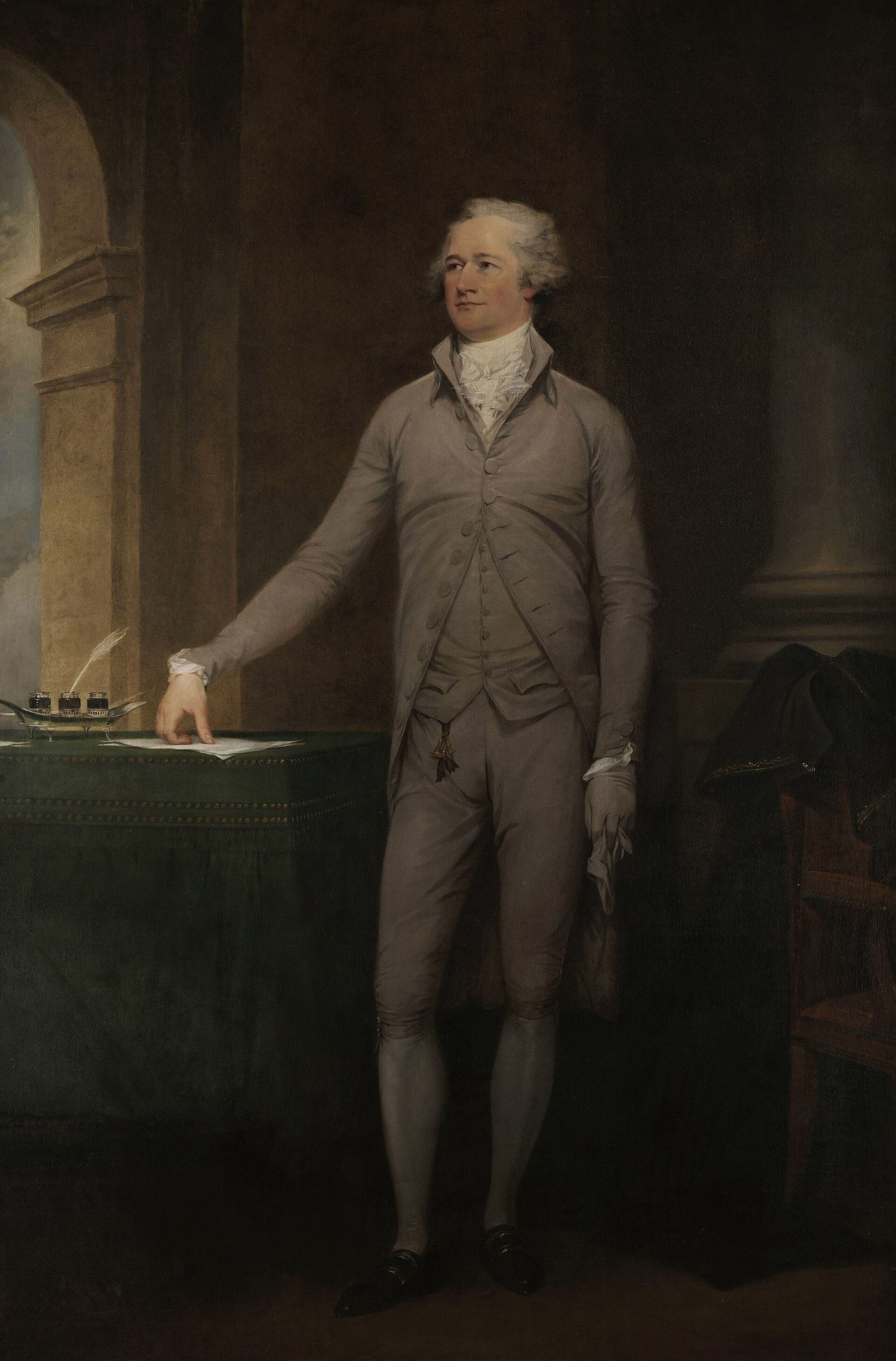 Full-length oil portrait of a slight man in a pale grey suit standing beside a green-draped table, one hand resting on a sheet of paper next to a silver inkstand holding a quill, a dark cloak and cocked hat on a chair behind him