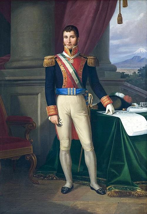 Portrait of a Mexican military officer in formal dress uniform with gold epaulettes, sash, and decorative medals, standing at a desk with documents.