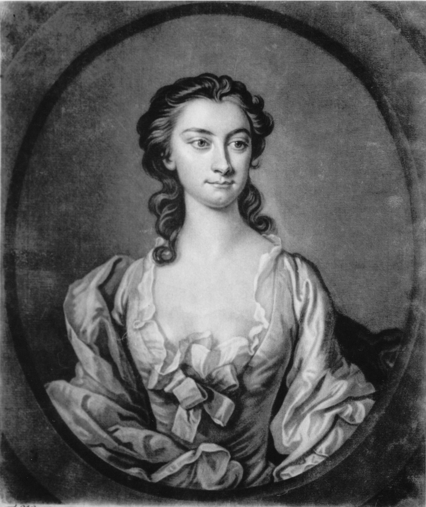 Black-and-white oval portrait of a young woman with dark curled hair, in a loose satin gown with a bow at the bodice