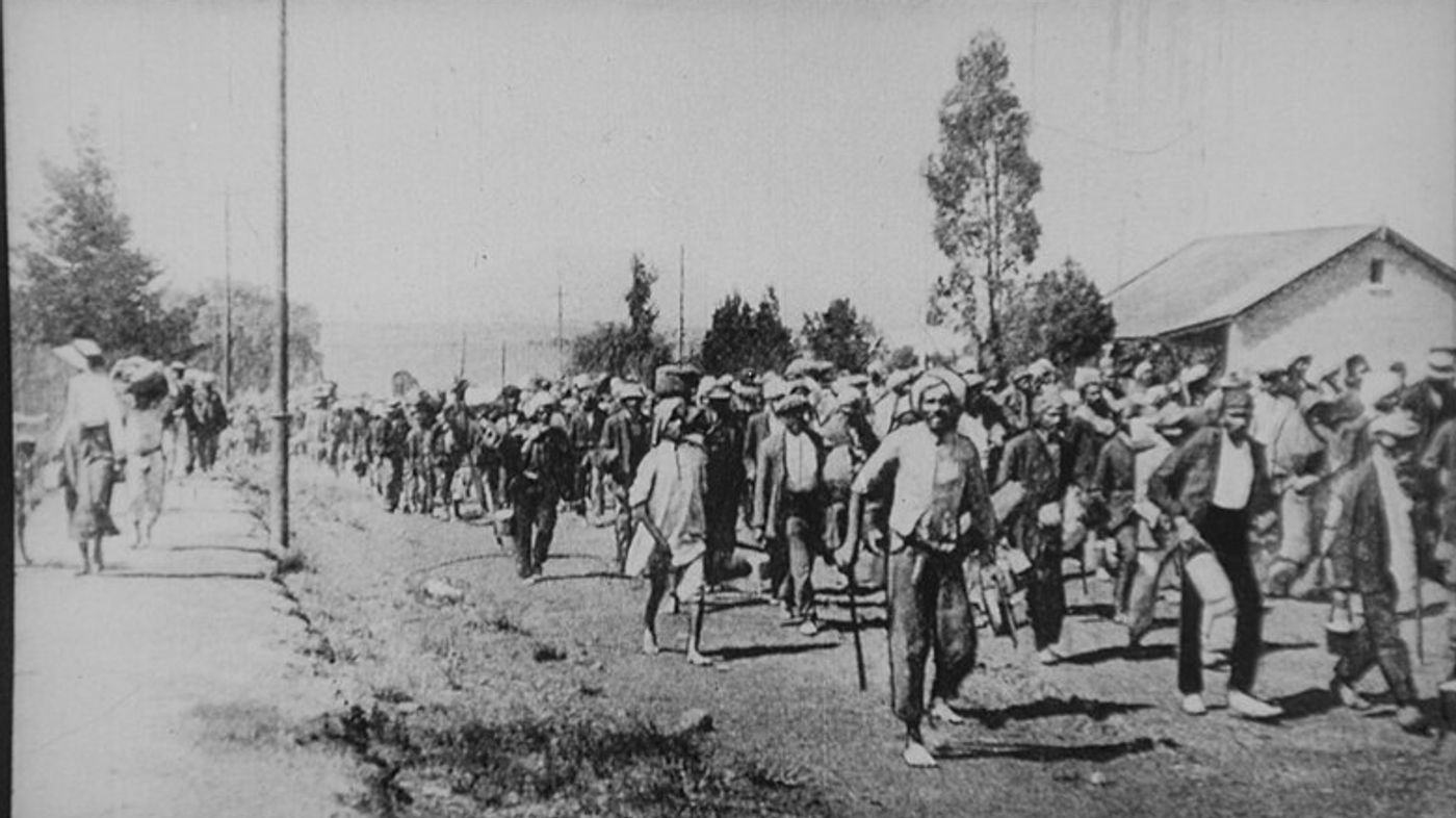 Large crowd of people marching on a dirt road lined with trees and buildings, labeled "The Great March."