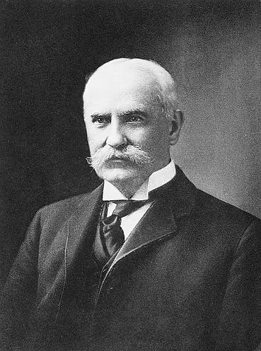 Black and white portrait photograph of Nelson Aldrich with white hair and mustache wearing a dark suit and striped tie.