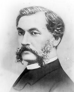 Black and white portrait photograph of a bearded man in formal attire with a white collar, circa early 20th century.