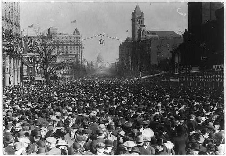 Massive crowd gathered on city street celebrating women's suffrage, circa 1920s, with historic buildings and church spire visible.