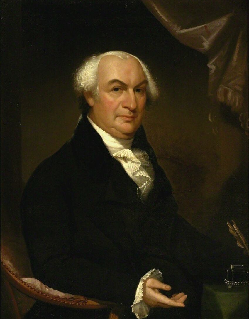 Oil portrait of Gouverneur Morris seated in a dark coat and white stock, grey hair swept back from a high forehead, one hand resting on the arm of a chair beside a green-covered table