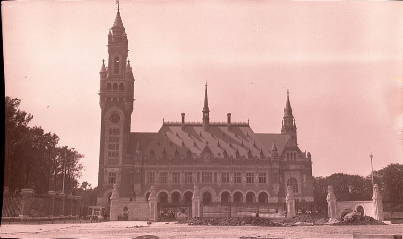 Peace Palace in The Hague with prominent clock tower and Gothic Revival architecture, surrounded by manicured gardens and gates.