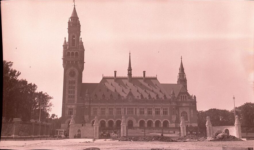Peace Palace in The Hague with prominent clock tower and Gothic Revival architecture, surrounded by manicured gardens and gates.