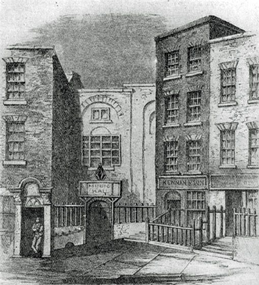 Engraving of a narrow street with tall brick buildings on either side of a recessed hall with an arched doorway and a railed forecourt