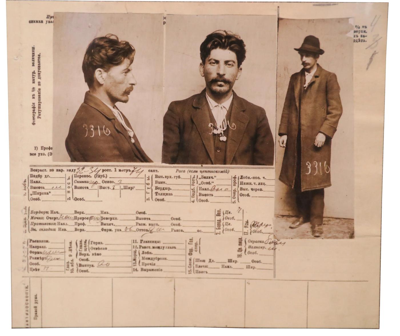 An official police card with three photographs of a young man with dark hair and a moustache, in profile, facing front, and standing in a long coat and hat, above a handwritten table of details