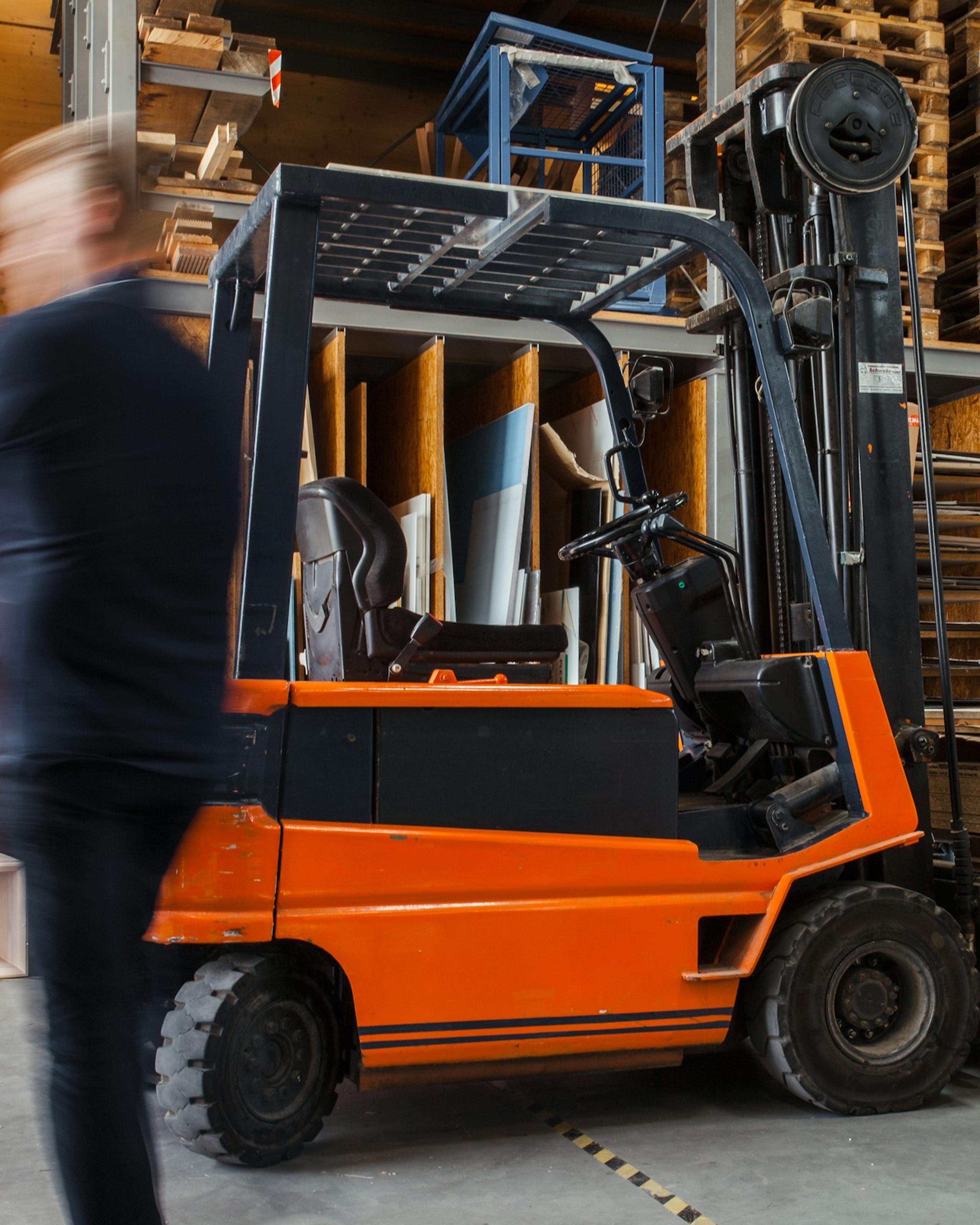 Worker on foot passing a forklift in a warehouse, where forklift traffic is a common source of warehouse injury claims