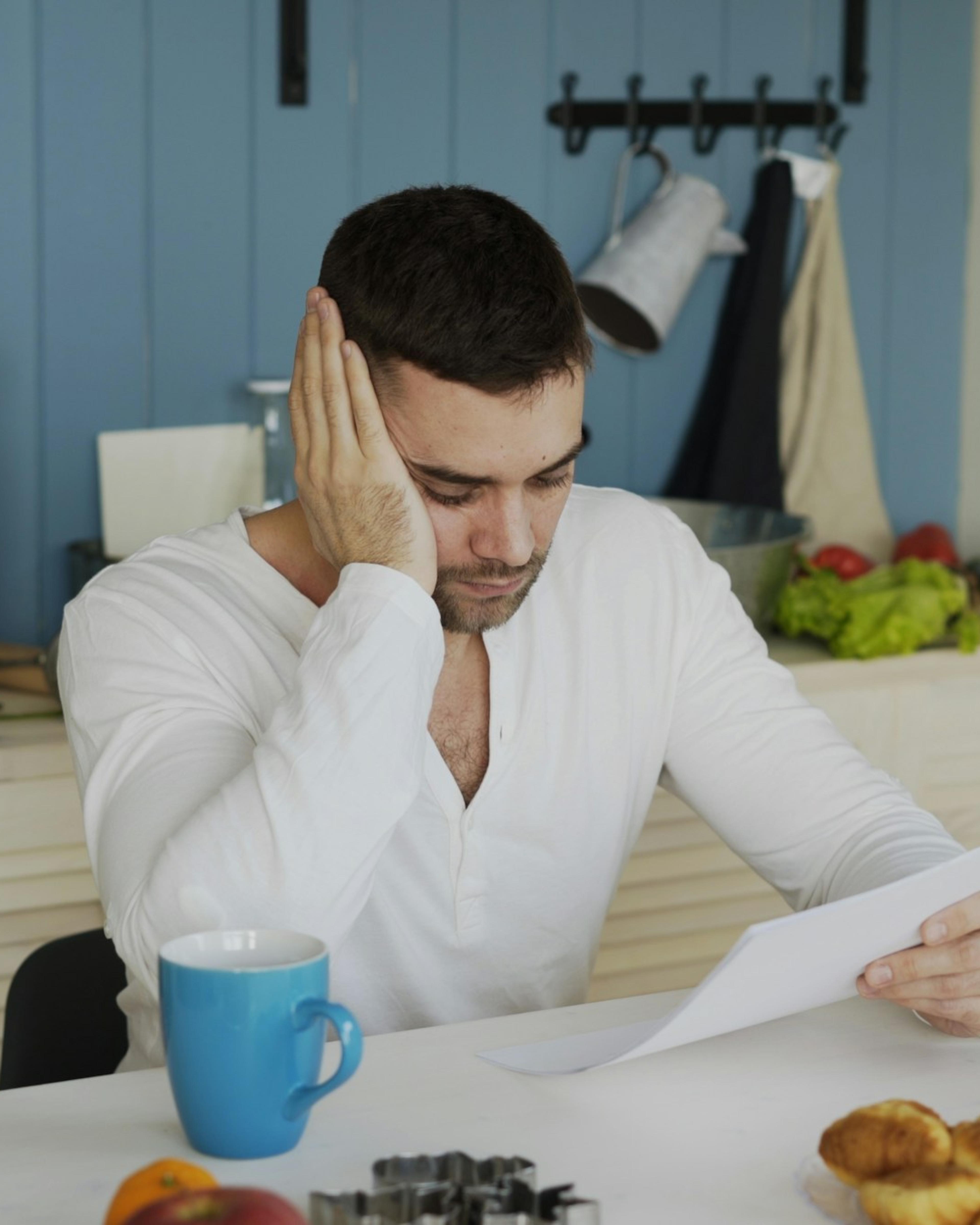 Hombre preocupado leyendo una carta en la mesa de su cocina, un momento que conocen muchos trabajadores que sufren represalias