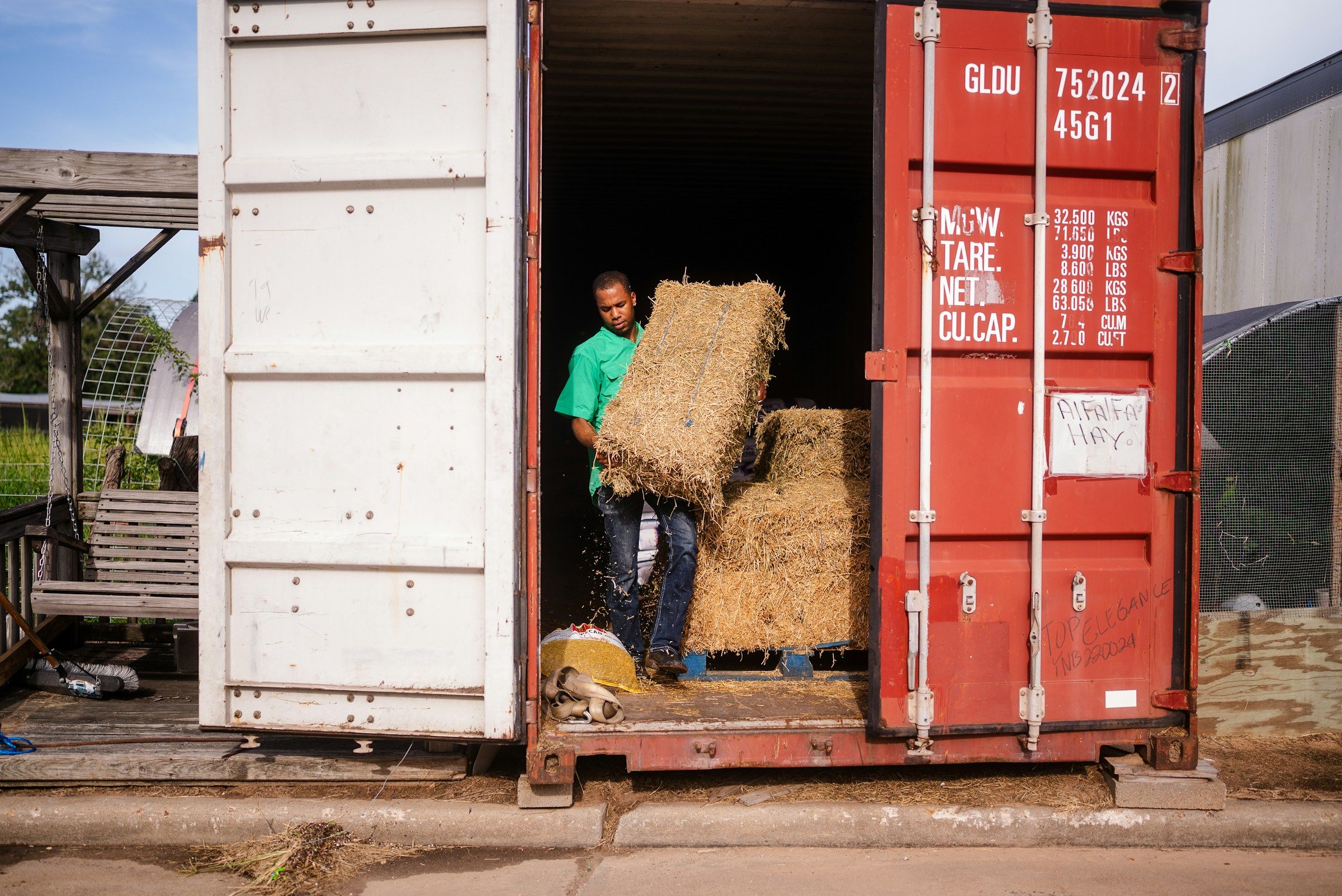 Worker lifting a heavy hay bale out of a shipping container, the kind of strain behind many back injury workers’ comp claims
