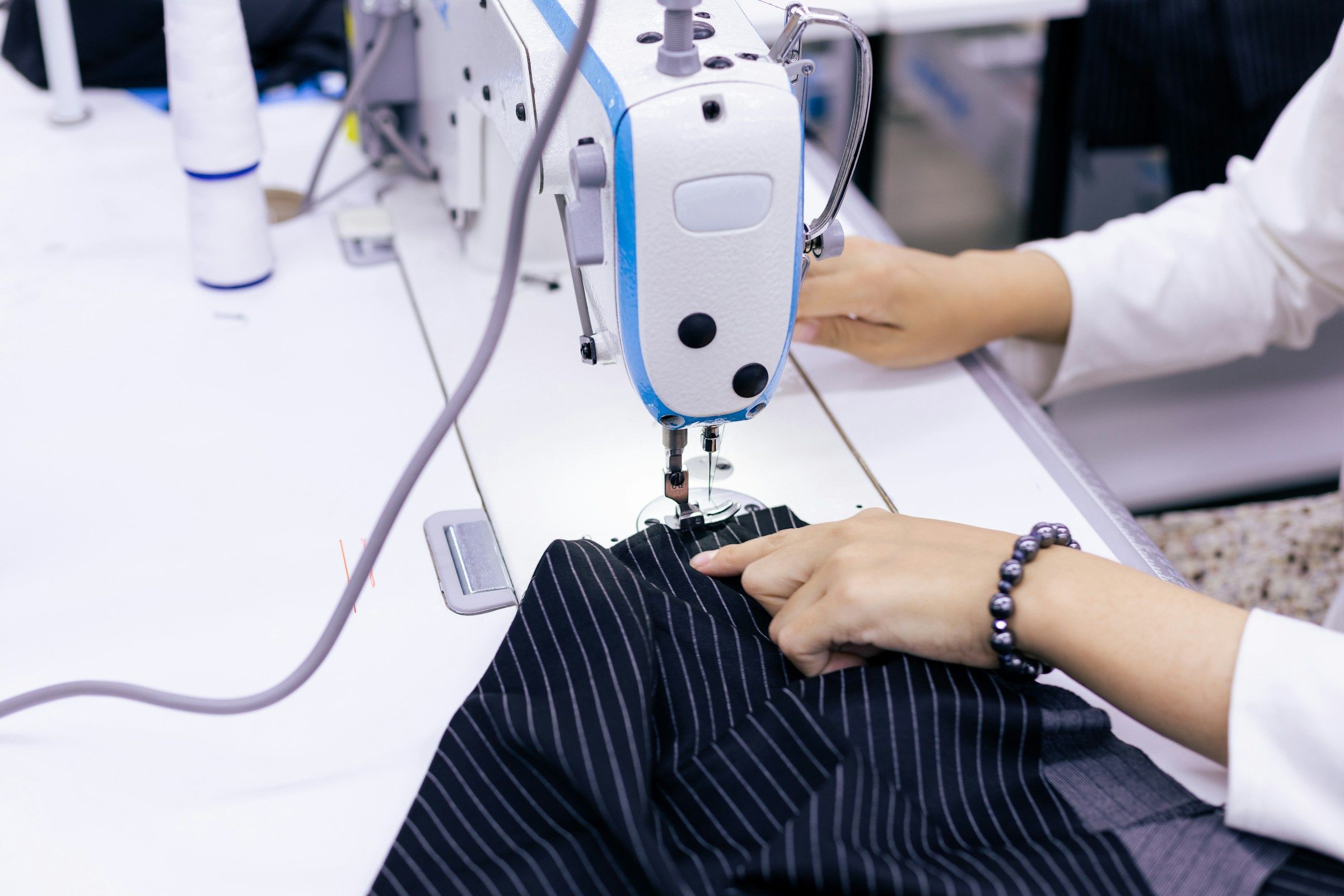 Hands guiding fabric through an industrial sewing machine, repetitive work that can lead to a repetitive stress injury workers’ comp claim