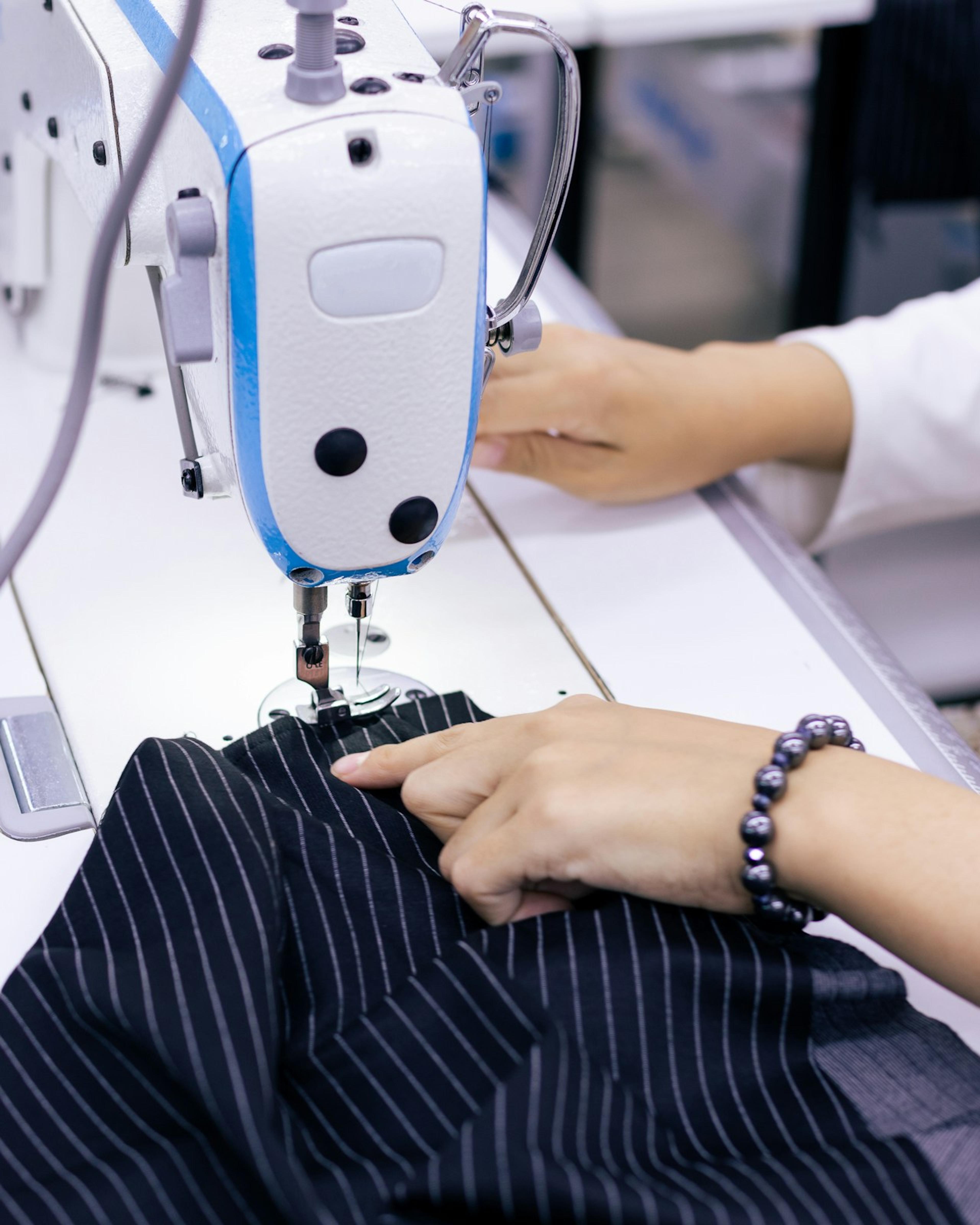 Hands guiding fabric through an industrial sewing machine, repetitive work that can lead to a repetitive stress injury workers’ comp claim