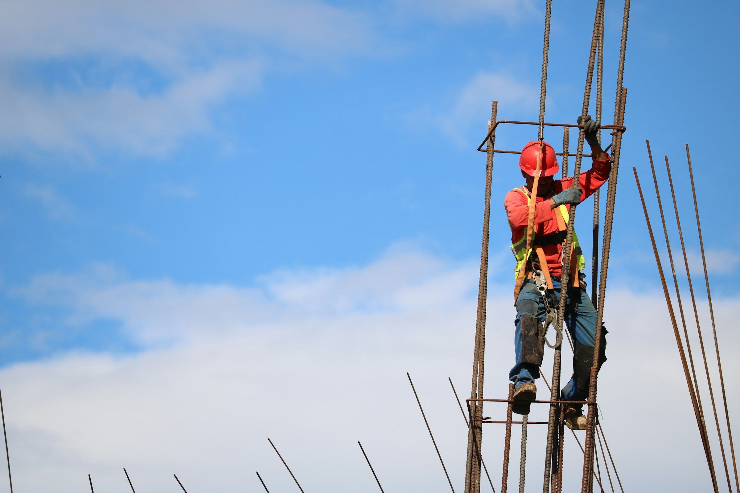 Worker in a hard hat and harness climbing a rebar cage high above the ground, the kind of work behind many construction accident workers’ comp claims