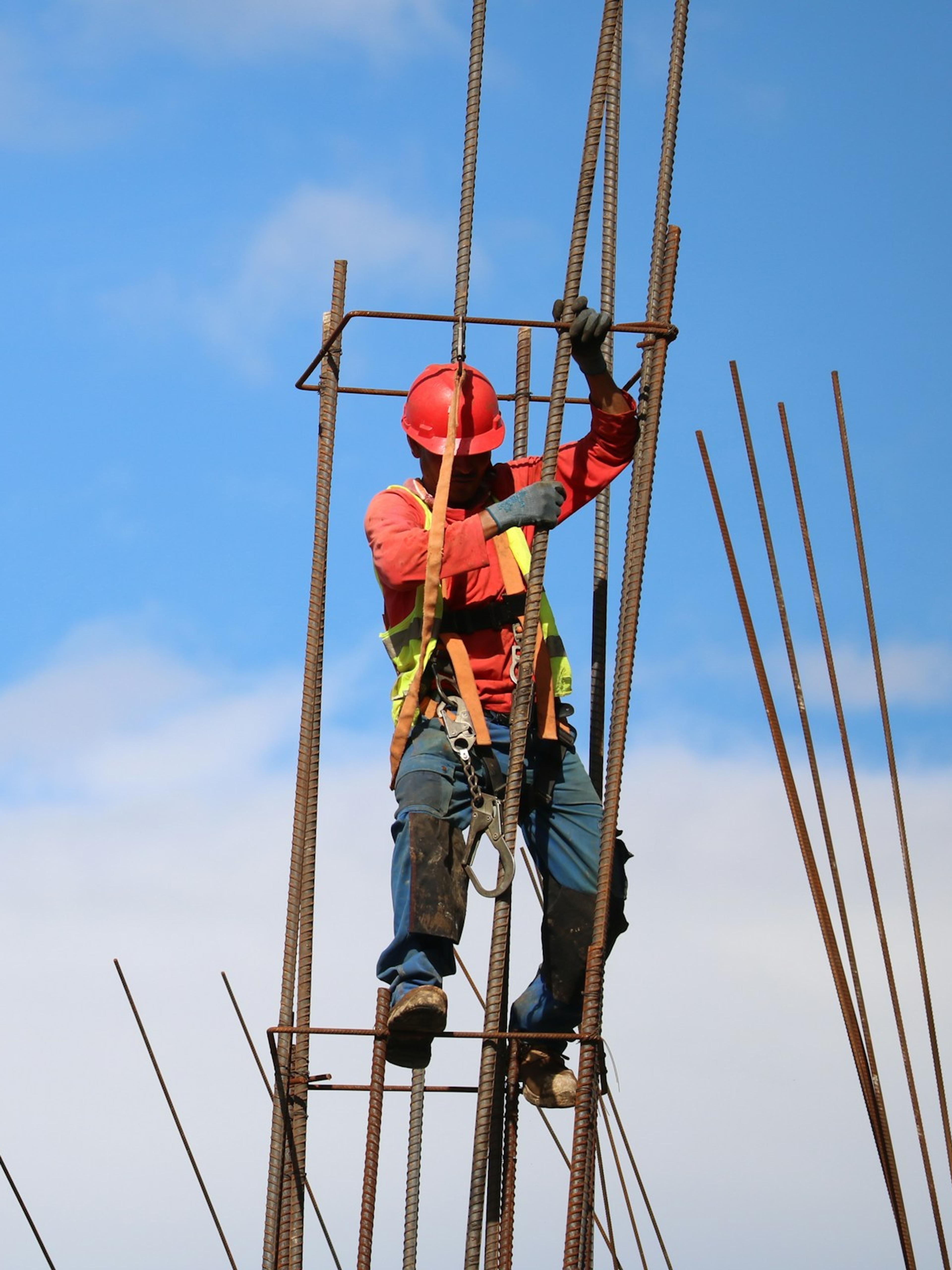 Worker in a hard hat and harness climbing a rebar cage high above the ground, the kind of work behind many construction accident workers’ comp claims