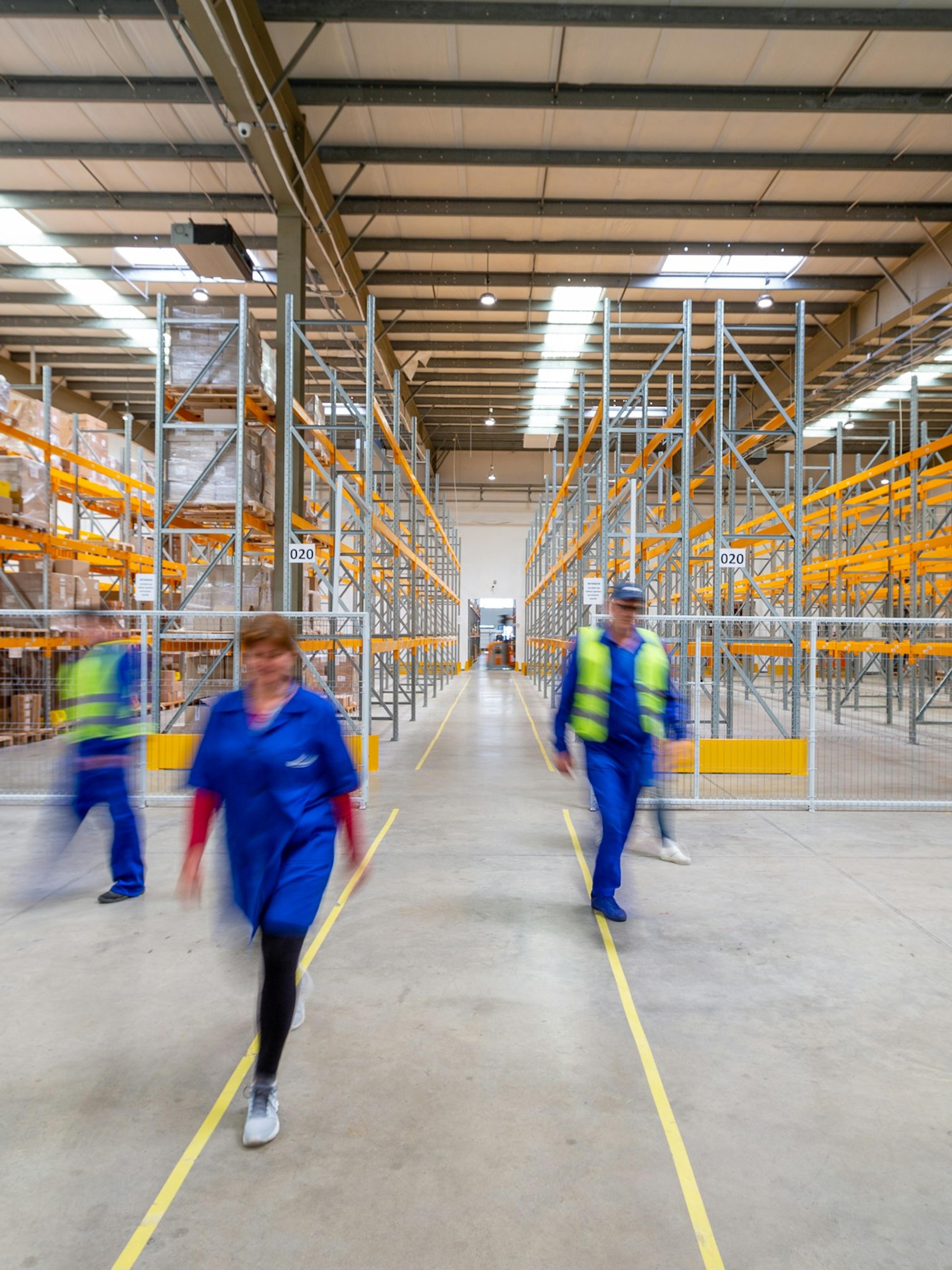 Warehouse workers hurrying down an aisle between pallet racks, the fast-paced work behind many cases a warehouse injury lawyer sees