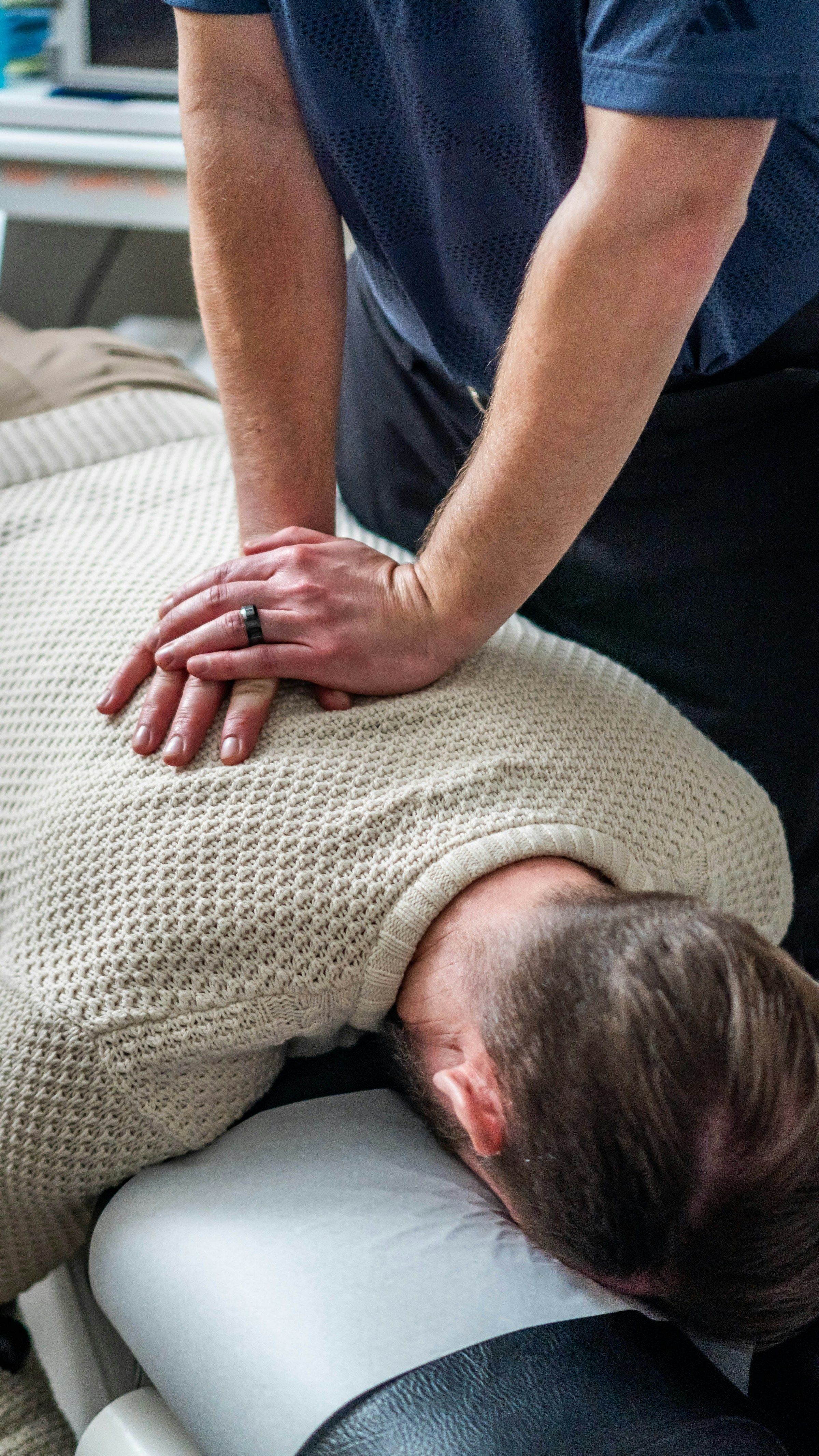 Chiropractor pressing on a patient’s upper back, one of the treatments workers’ comp can cover for a back injury