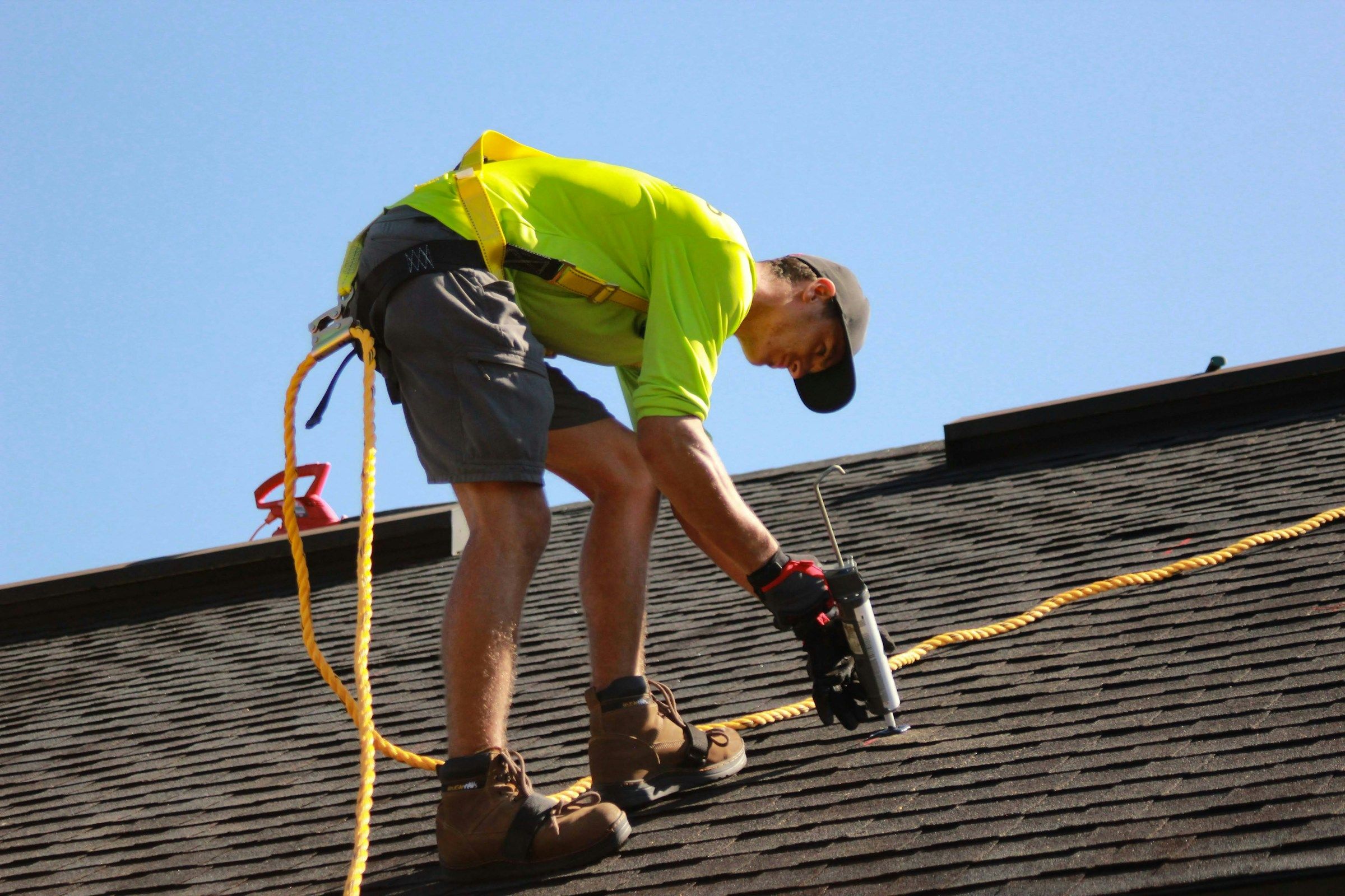 Roofer bending with knees flexed on a sloped roof, the kind of strain behind many knee injury workers’ comp claims