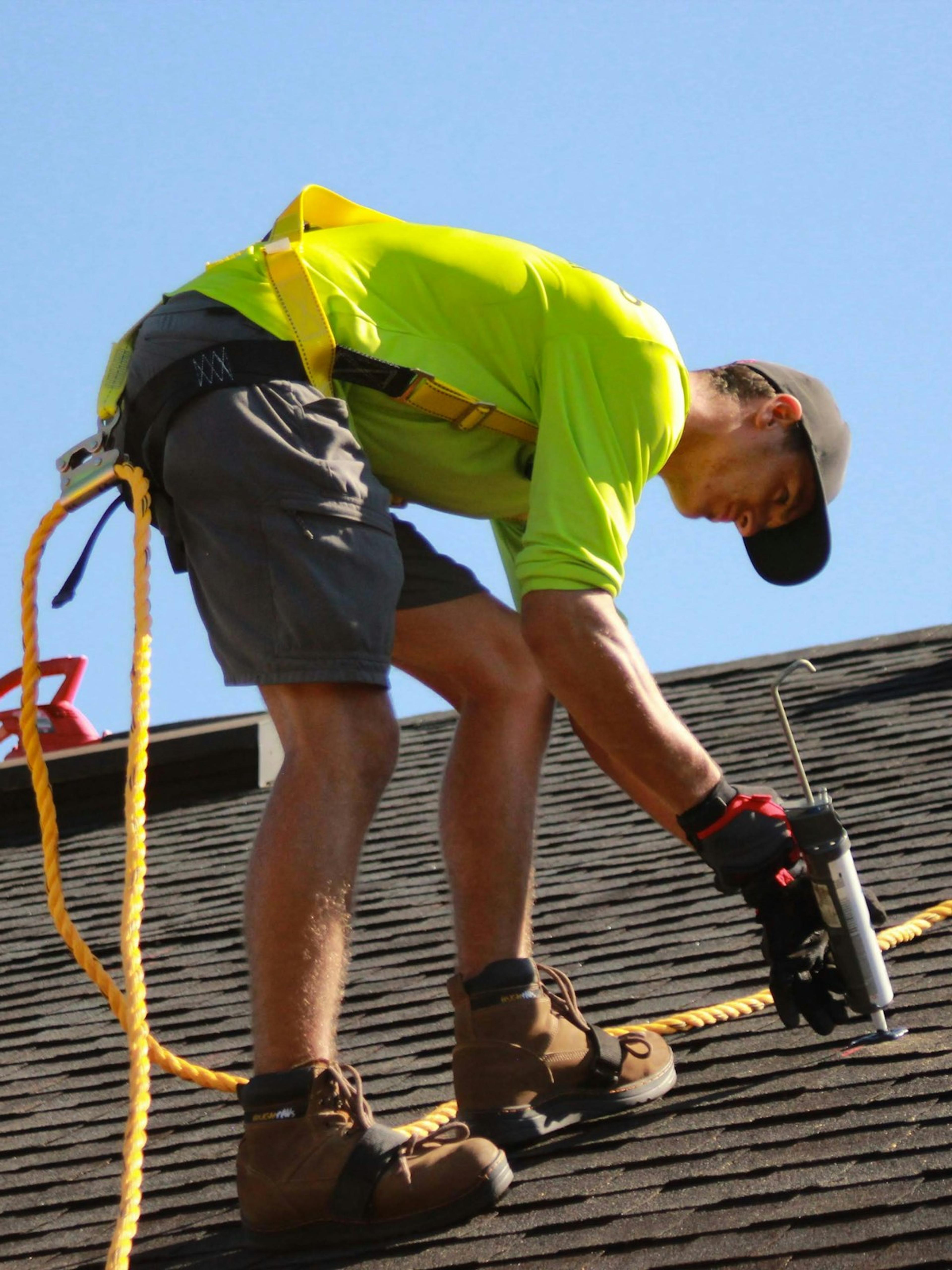 Roofer bending with knees flexed on a sloped roof, the kind of strain behind many knee injury workers’ comp claims