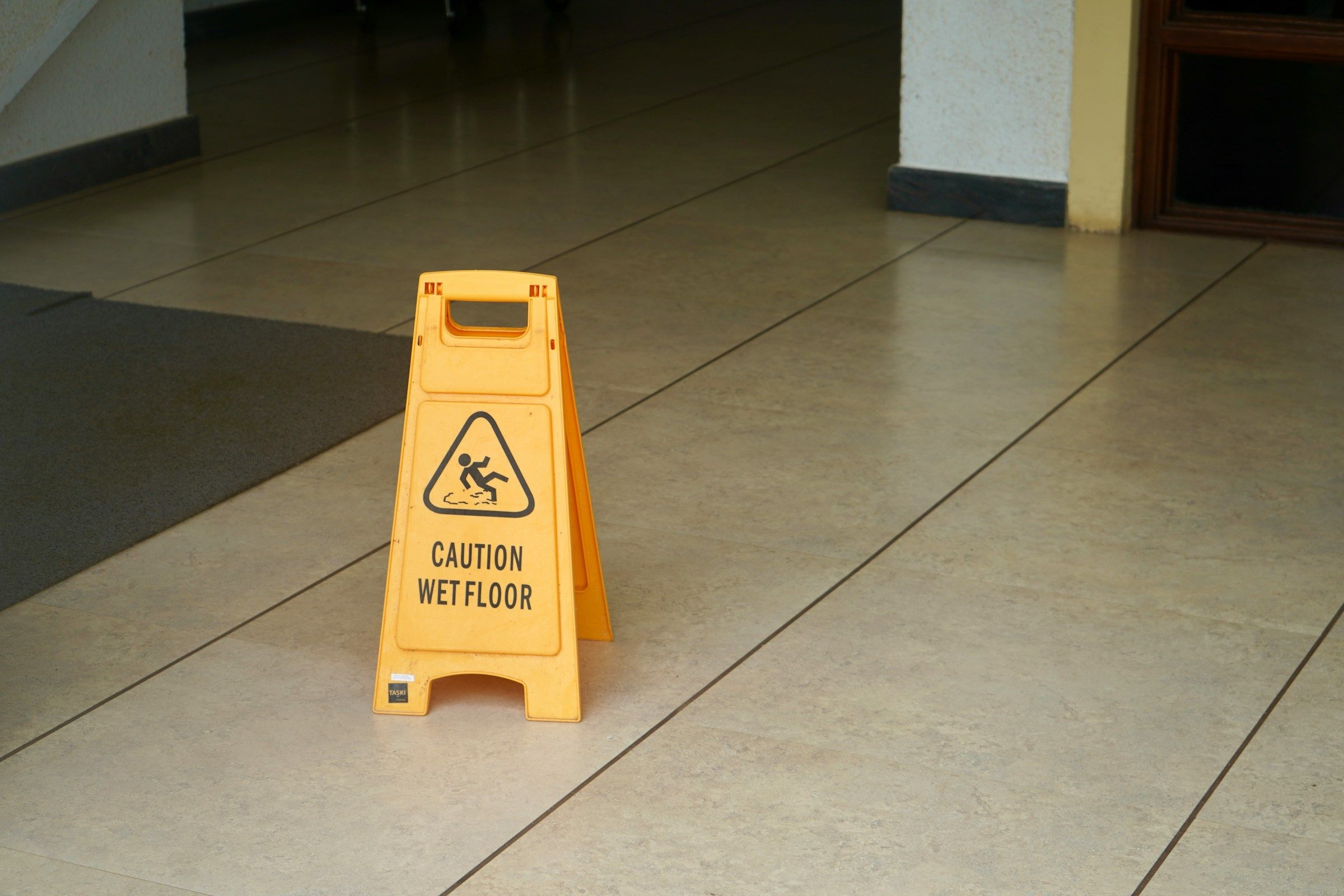 Letrero amarillo de piso mojado en un pasillo de baldosas, un peligro común en los resbalones y caídas en el trabajo