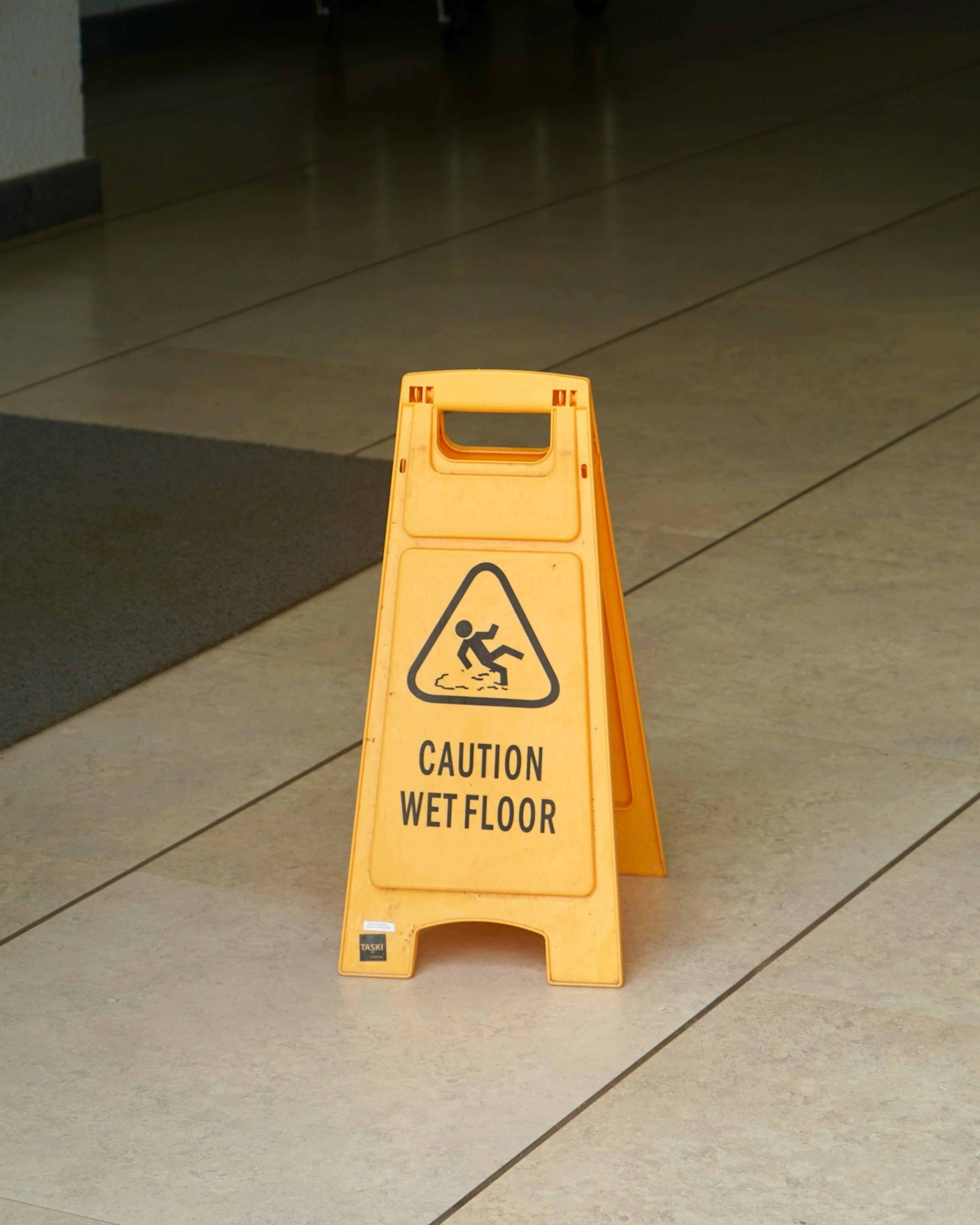 Yellow caution wet floor sign on a tiled hallway, a common hazard in slip and fall at work claims