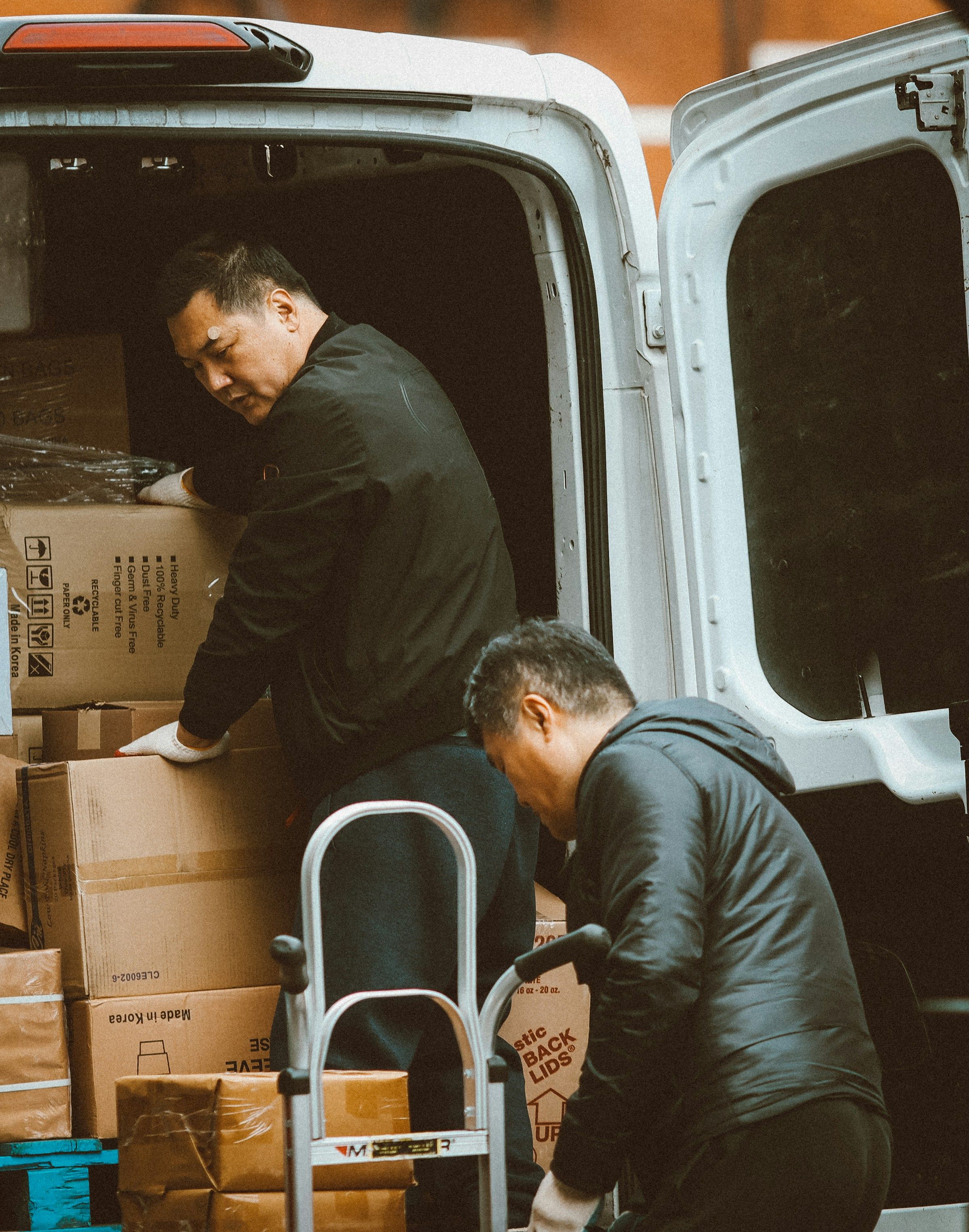 Two delivery workers unloading heavy boxes from a van onto a hand truck, the lifting behind many delivery driver workers’ comp claims